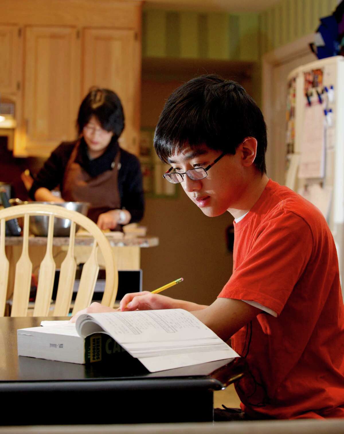 Howard Ho, 18, works on his calculus while his mother Sandy Ho prepares dinner in their New Milford, Conn, home. Ho is home schooled and has been applying to colleges for the fall. He has already started taking classes at Western Connecticut State University. Tuesday, January 14, 2014.