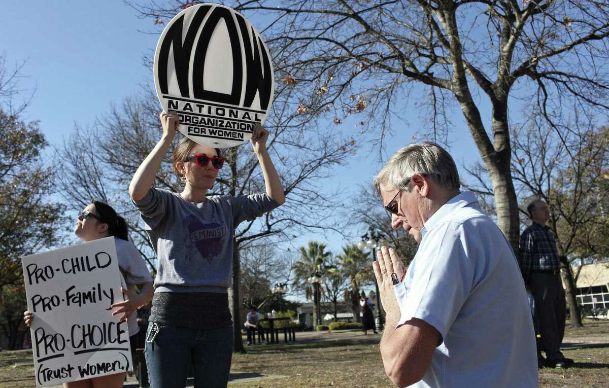 Guy McClung, 66, who is against abortion, prays in front of abortion rights supporters Mitsue McCoy, 28, president of the San Antonio chapter of the National Organization for Women (center) and Jennifer Falcon, 30, San Antonio lead organizer for GetEQUAL Texas, during the San Antonio Right to Life Foundation's rally in Milam Park.