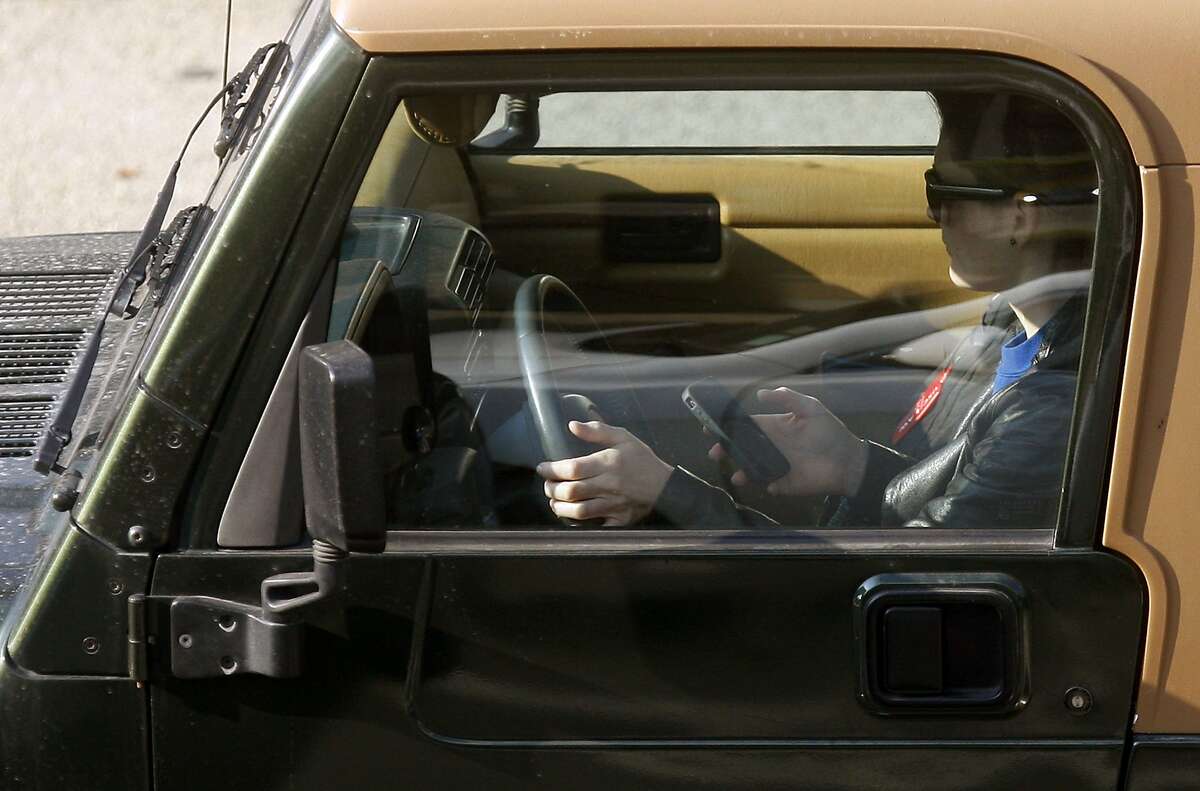 In this Wednesday, Dec. 14, 2011, file photo, a driver uses an iPhone while driving Wednesday, in Los Angeles. The country's four biggest cellphone companies are set to launch their first joint advertising campaign against texting while driving, uniting behind AT&T's "It Can Wait" slogan to blanket TV and radio during the summer of 2013. (AP Photo/Damian Dovarganes, File)