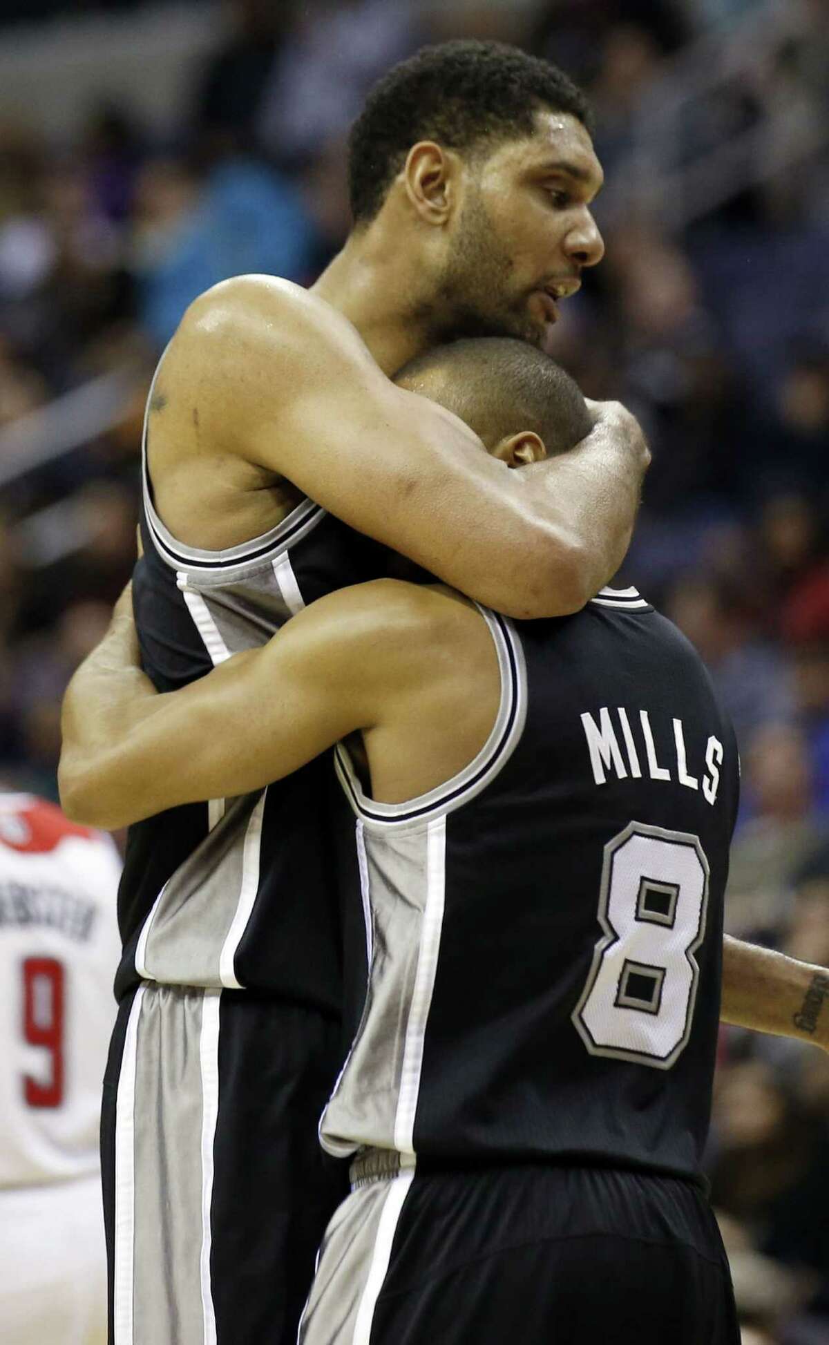 San Antonio Spurs forward Tim Duncan, top, embraces guard Patty Mills (8), from Australia, during a timeout in the first overtime of an NBA basketball game against the Washington Wizards, Wednesday, Feb. 5, 2014, in Washington. Duncan had 31 points and Mills had 23 in their 125-118 double overtime win. (AP Photo/Alex Brandon)