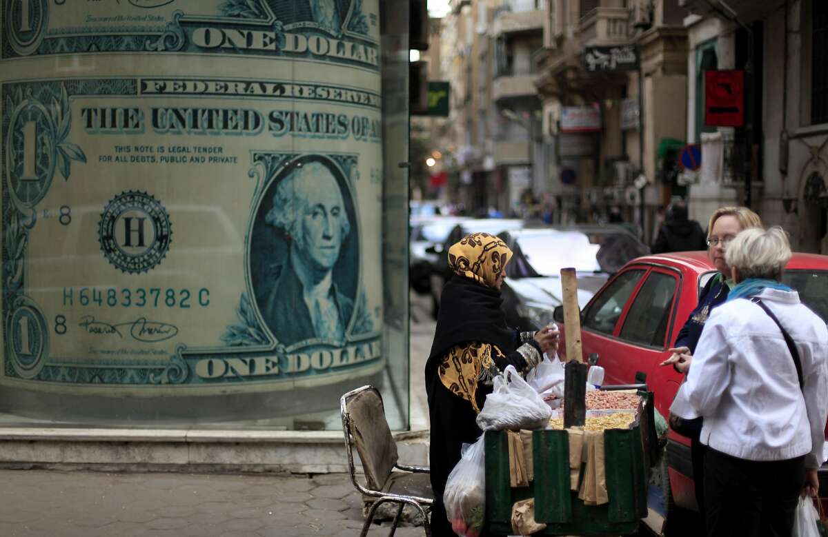 An Egyptian vendor sells nuts in front of a giant poster of a U.S. dollar outside a currency exchange office in Cairo, Egypt, Tuesday, Dec. 25, 2012. As Egypt prepared to release official results from the constitutional referendum, its economy showed increasing signs of distress on Tuesday with worried residents hoarding dollars and fearing that continued political instability will lead to a fast devaluation of the local currency. The Central Bank of Egypt said Tuesday that the U.S. dollar was selling at 6.18 to the Egyptian pound, a spike from the rate of six pounds just two months ago. (AP Photo/Khalil Hamra)