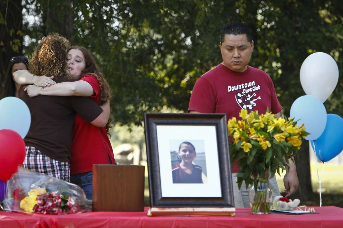 Hannah Turpin, 13, (left), a classmate and friend of Asher Brown, gives Amy Truong, Asher's mother, a hug as her husband David Truong (right), reflects as he looks towards a photo of his stepson, Asher Brown, the thirteen-year-old boy who committed suicide as a result of school bullying last week, during a memorial service near Moore Elementary School Saturday, Oct. 2, 2010, in Houston. Asher shot himself in the head with his stepfather's handgun on Sept. 23 at his family's home. Truong said his son, a straight-A student who loved to read, had been ridiculed by students at school because he was small, a Buddhist and didn't wear designer clothes. "What my child went through was not normal in any capacity," Truong said. "It was relentless. It was just day after day and nothing was done and now my son is dead." ( Michael Paulsen / Houston Chronicle )