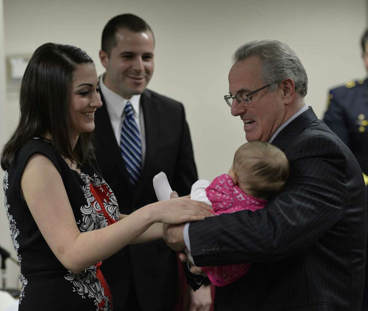 Troy Mayor Lou Rosamilia holds baby Callihan, daughter of Ryan MacDonald, center, and Jordan MacDonald, left, so that Jordan can pin Ryan's police shield on his jacket after being sworn in as a new member of the Troy Police Friday afternoon, Feb. 14, 2014, in Troy, N.Y. (Skip Dickstein/ Times Union)