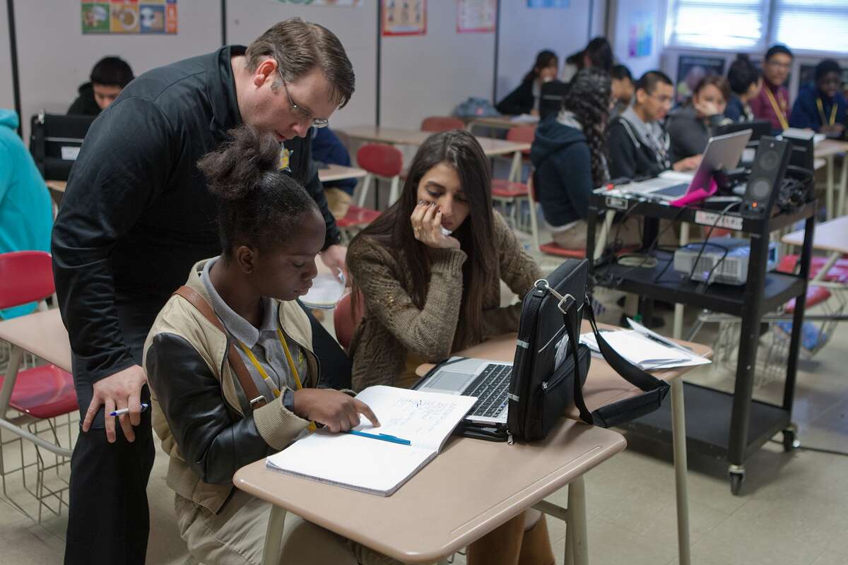 Instructor Ed Jones checks in on Laverne Dilder, 16, left, and Aisha Ahmed, 17, as they work using Dilder's new laptop issued through the PowerUp program.