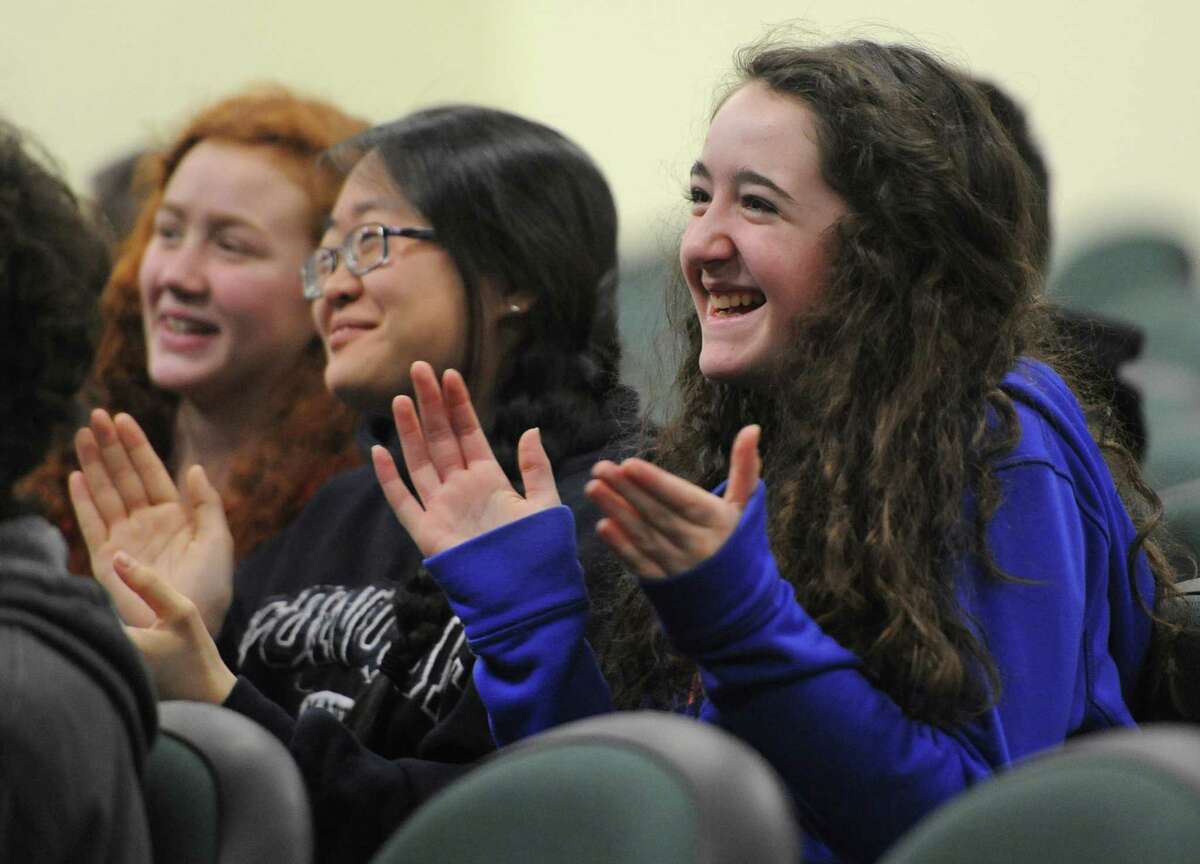 Seventh-graders Sarah Widman, left, Alex Bayuk, center, and Erin Walsh give a round of applause during the assembly showing students the water well in Liberia they helped fund through their push cart fundraiser, at Newtown Middle School in Newtown, Conn. Thursday, Feb. 20, 2014. The group of Reed Intermediate School students raised $2,800 in one day, which was enough to build a well and bring clean drinking water to students at New Life Academy in Liberia.