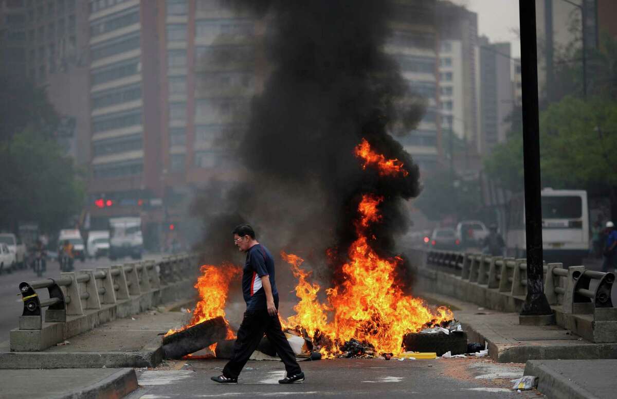A pedestrian walks in front of a burning barricade blocking the highway in Chacao, Caracas, Venezuela, Monday, Feb. 24, 2014. Traffic has come to a halt in parts of the Venezuelan capital because of barricades set up by opposition protesters across major thoroughfares. The protests are part of a wave of anti-government demonstrations that have swept Venezuela since Feb. 12 and have resulted in at least 10 deaths. The protests in the capital Monday were peaceful. Police and National Guard troops stood by but did not act to remove the barricades despite the effect on the morning commute.