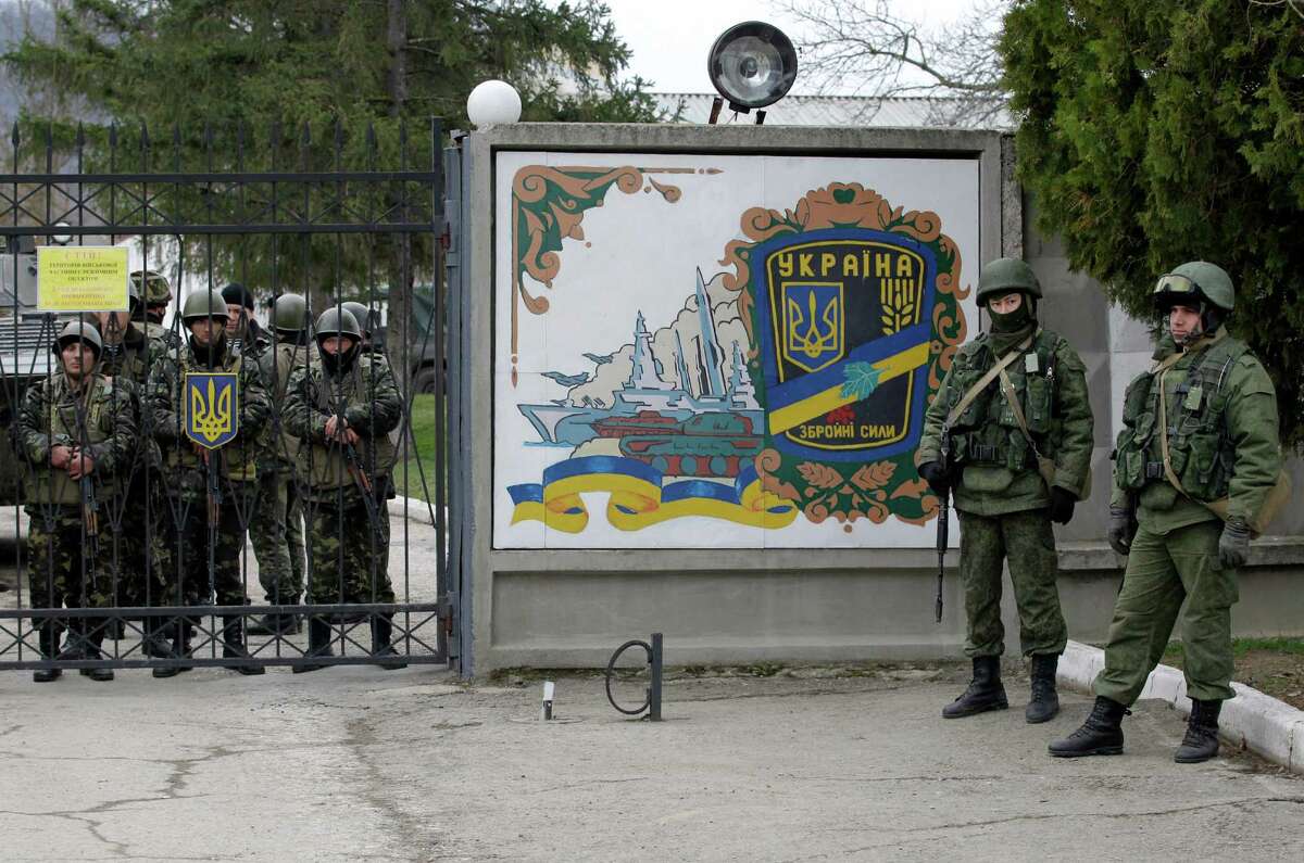 Ukrainian soldiers, left and unidentified gunmen, right, guard the gate of an infantry base in Privolnoye, Ukraine, Sunday, March 2, 2014. Hundreds of unidentified gunmen arrived outside Ukraine's infantry base in Privolnoye in its Crimea region. The convoy includes at least 13 troop vehicles each containing 30 soldiers and four armored vehicles with mounted machine guns. The vehicles â?” which have Russian license plates â?” have surrounded the base and are blocking Ukrainian soldiers from entering or leaving it. (AP Photo/Darko Vojinovic)