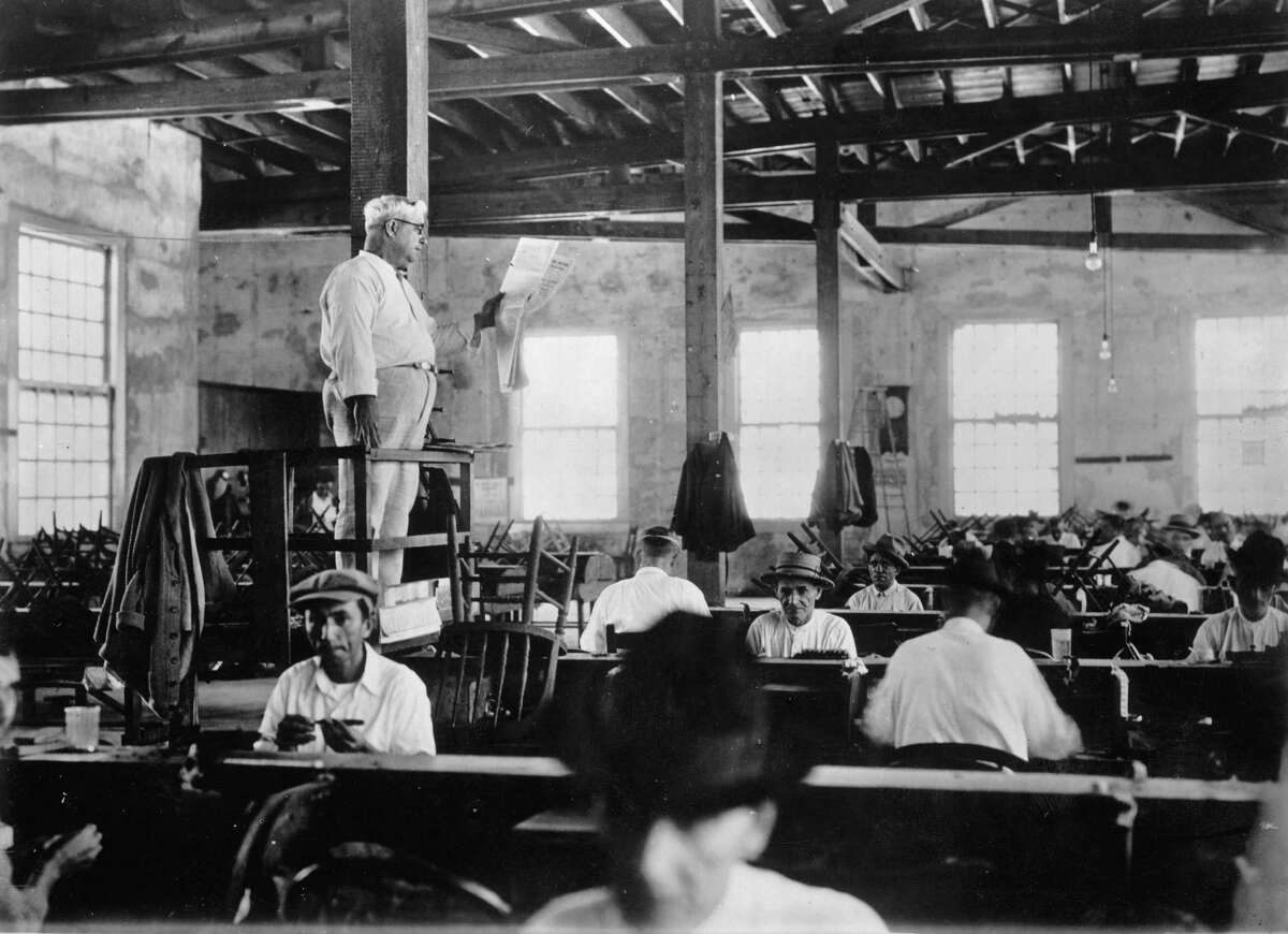 American factories sometimes employed guys like this, who stood or sat on elevated platforms and read books, newspapers and the like to the workers. Here, a newspaper reader entertains cigar rollers in Key West, Florida in 1930.