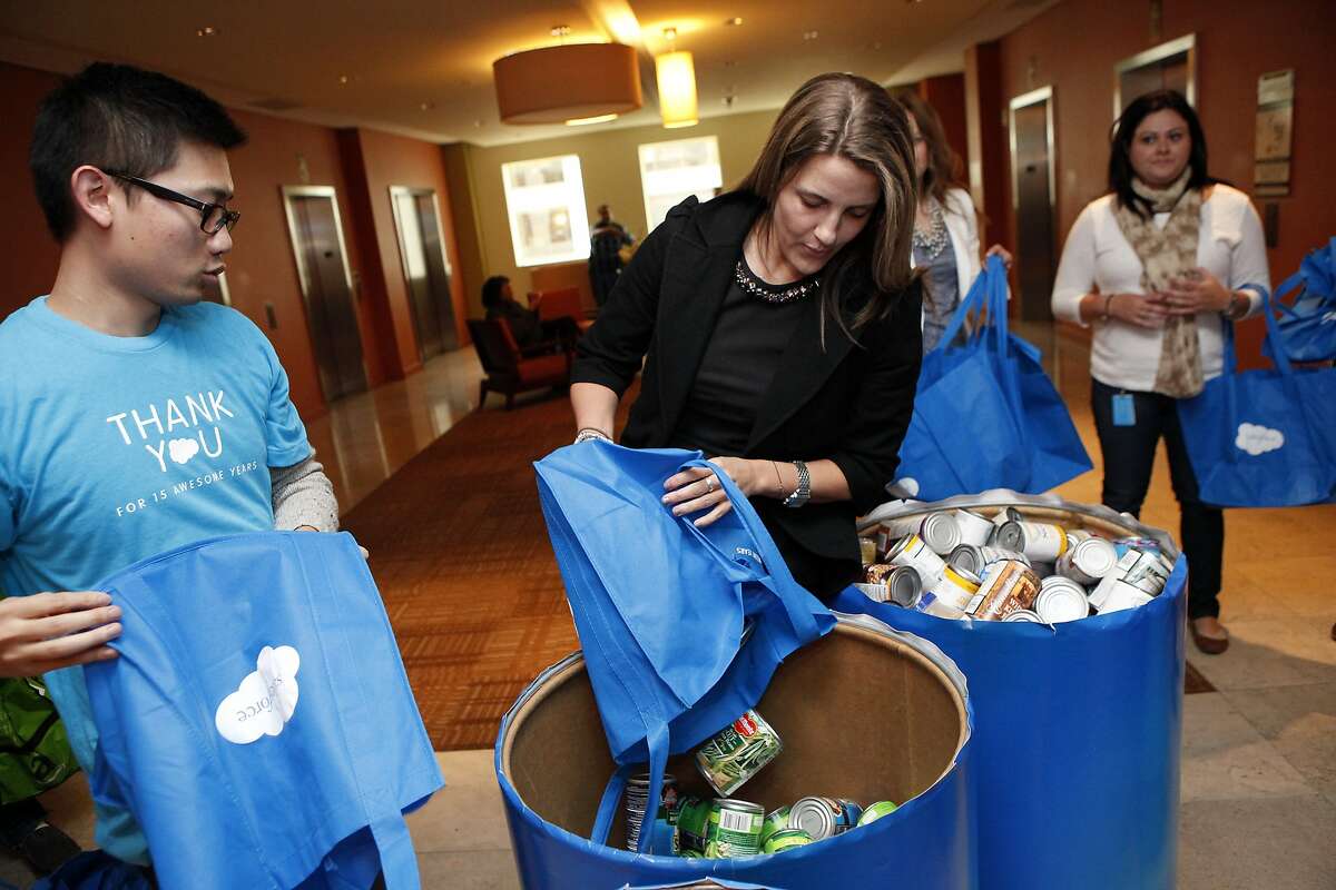 Salesforce.com employees Ernest Ng, left, helps Courtney Loomis dump her bag of canned food into a drum during a food drive at their Market St. offices in San Francisco, CA, Thursday, March 6, 2014.
