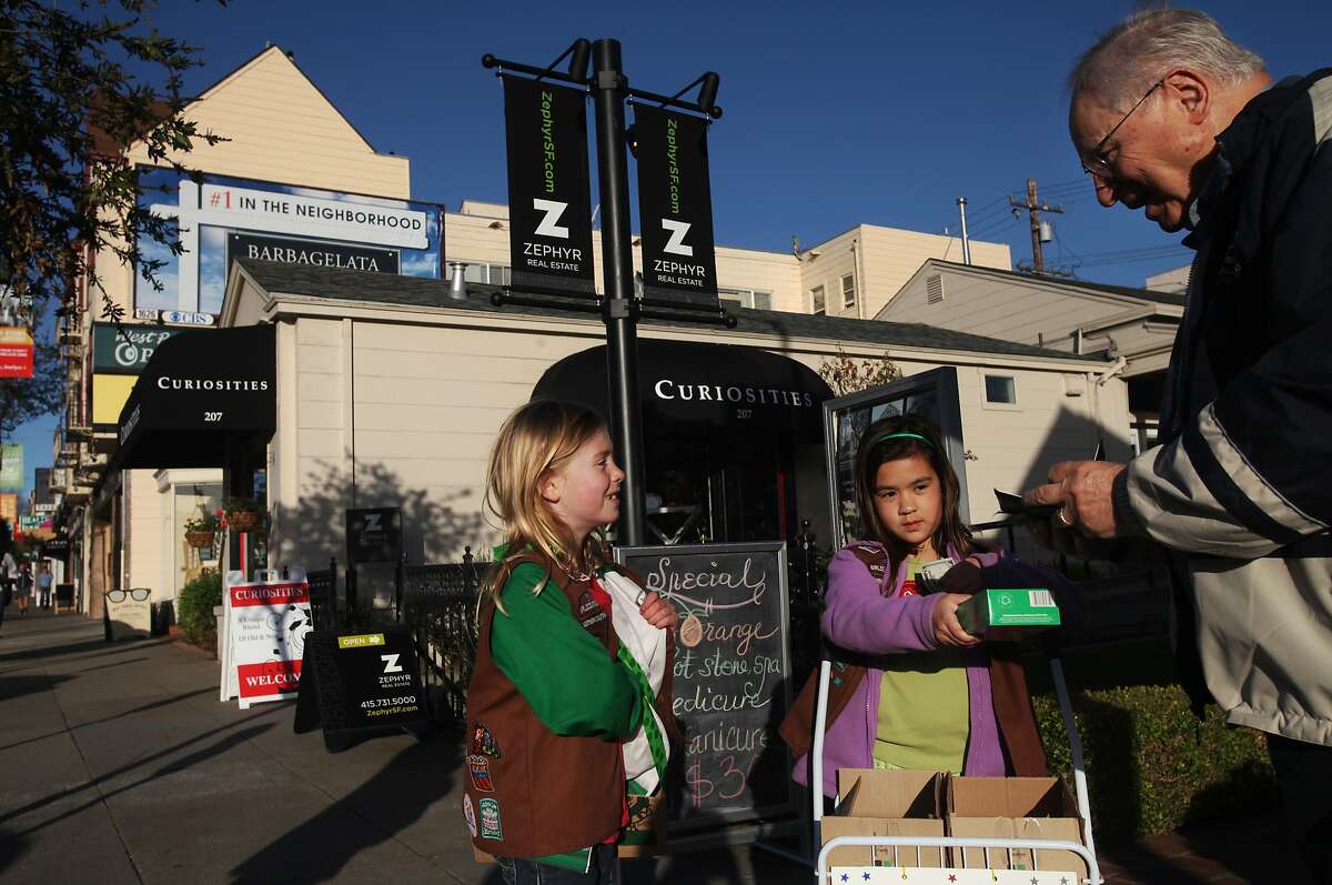 Paul Kameny buys Girl Scout cookies from Meghan Sheehan, 8, left, and Charlotte Jiggens, 7, March 7, 2014 on West Portal Ave. in San Francisco, Calif. Amy Nachman, who has been living in the neighborhood for 12 years loves it, "it's like a village within the city," she said.