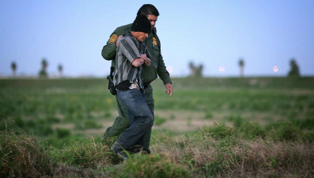 A Customs and Border Patrol officer walks apprehends an immigrant from Guatemala who was found hiding in tall grass just south of the border wall near Weslaco. ﻿