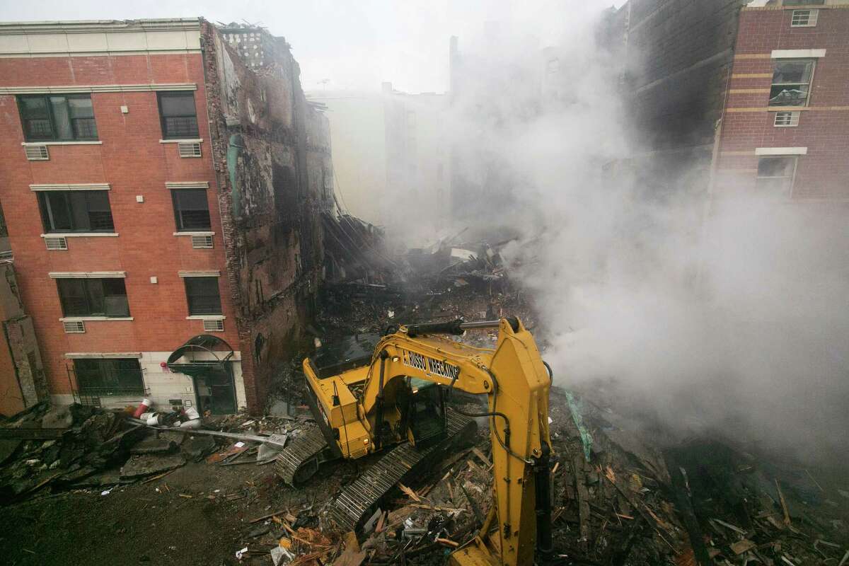 An excavator works to remove debris from the site of a building explosion, Thursday, March 13, 2014 in New York. Rescuers working amid gusty winds, cold temperatures and billowing smoke pulled four additional bodies Thursday from the rubble of two New York City apartment buildings, raising the death toll to at least seven from a gas leak-triggered explosion that reduced the area to a pile of smashed bricks, splinters and mangled metal. The explosion Wednesday morning in East Harlem injured more than 60 people. (AP Photo/Mark Lennihan) ORG XMIT: NYML112