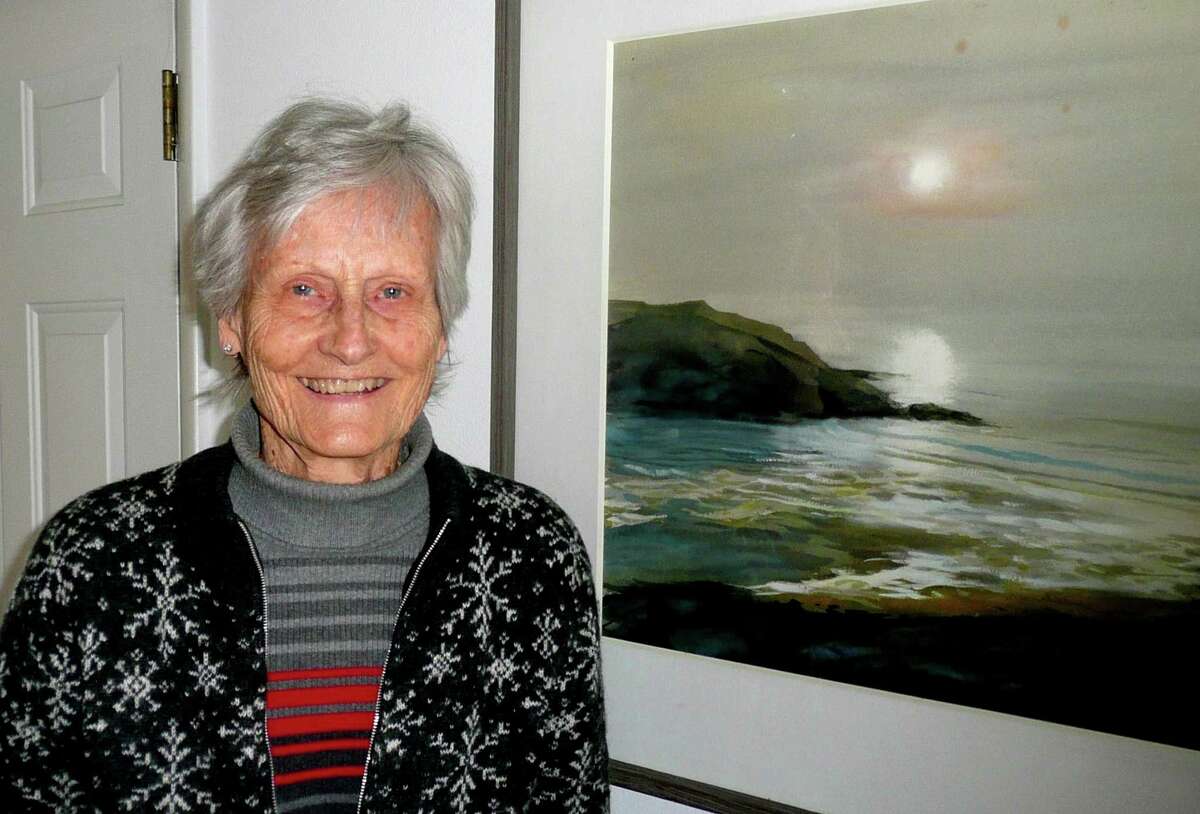 Polly Memhard, who lives in Riverside, stands next to a seascape by one of her favorite artists, Hans Axel Walleen.