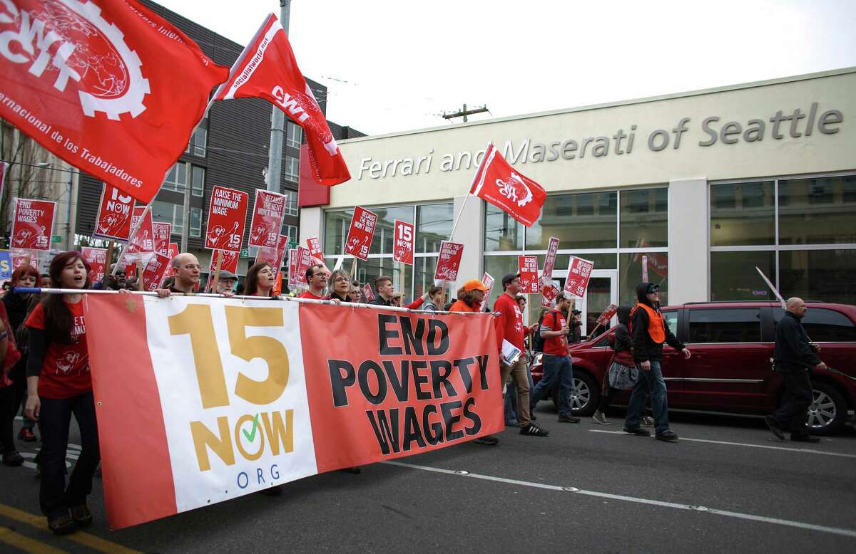 People march past an auto dealership in Capitol Hill during a march in Seattle to raise the minimum wage to $15 per hour. Hundreds of people marched from Judkins Park to Seattle Central Community College where a rally was held. Photographed on Saturday, March, 15, 2014.