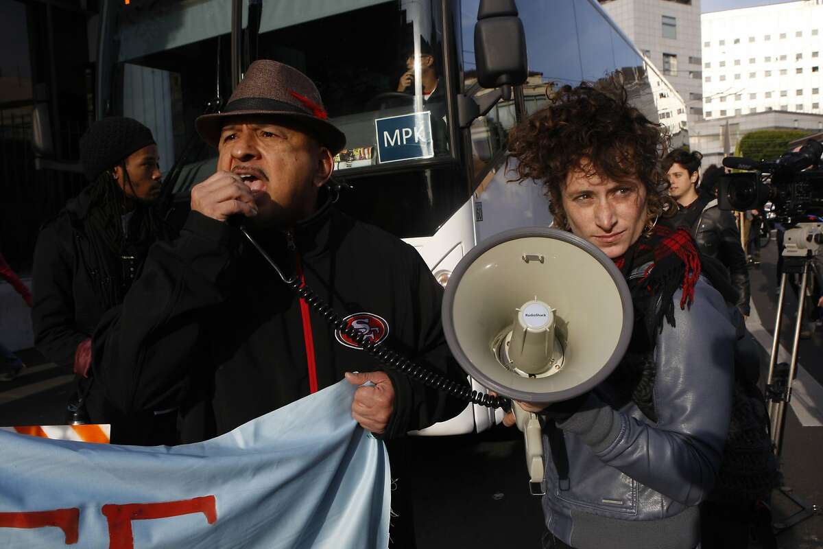 Activists Roberto Hernandez (left) and Erin McElroy (right) block a Facebook bus heading to Menlo Park on 8th at Market streets in San Francisco, Calif., on Tuesday, January 22, 2014. The San Francisco Metropolitan Transportation Agency votes on an 18-month pilot plan allowing Google buses to use designated Muni bus stops to pick up and drop off tech commuters to Silicon Valley.