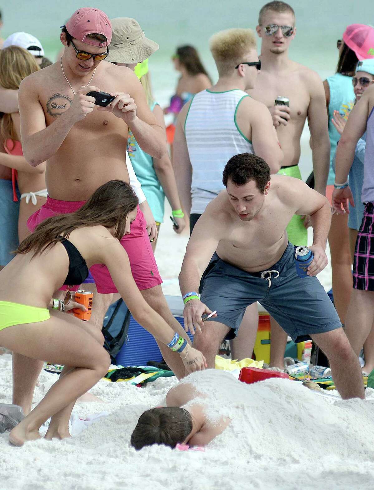 Spring breakers photograph their friend sleeping on the beach on Tuesday, March 18, 2014 in Destin, Fla.