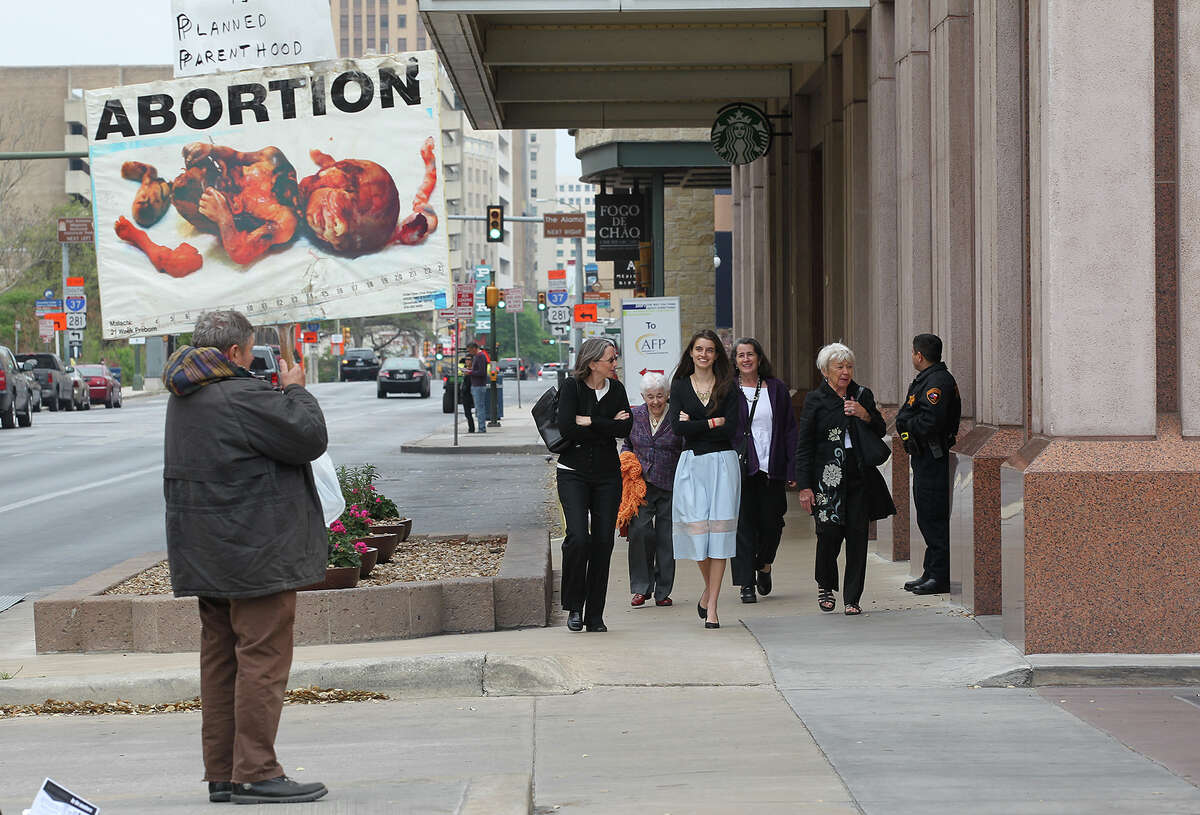 Pedestrians walk by anti-abortionists protesting a Planned Parenthood fundraiser luncheon at the Marriott Rivercenter Hotel, Monday, March 24, 2014. The featured speaker at the luncheon was actress Diane Keaton.