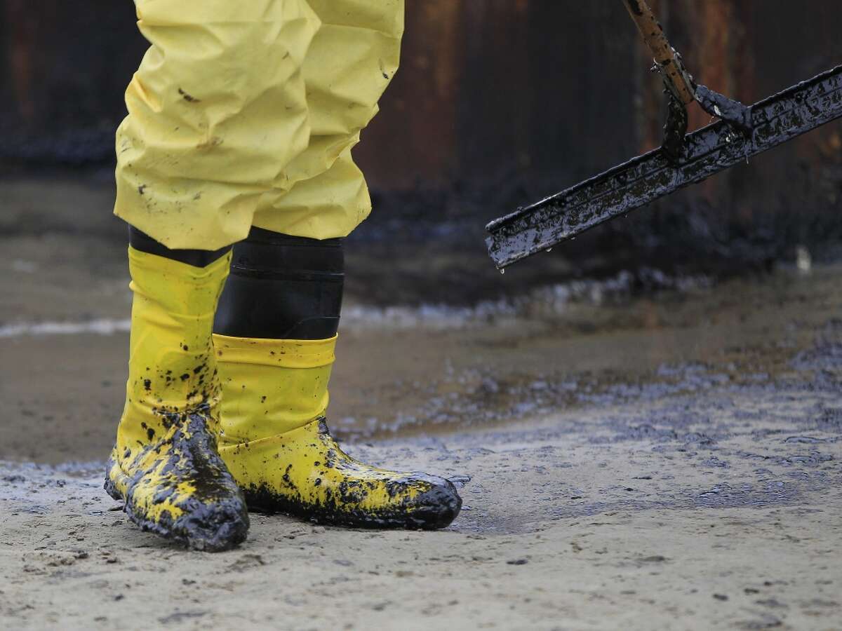 A worker gathers oil that spilled onto the sands of the Texas City dike at the site of the wrecked barge that leaked fuel into the Houston Ship Channel, Monday, March 24, 2014, in Texas City. Thousands of gallons of tar-like oil spilled into the major U.S. shipping channel after a barge ran into a ship Saturday.