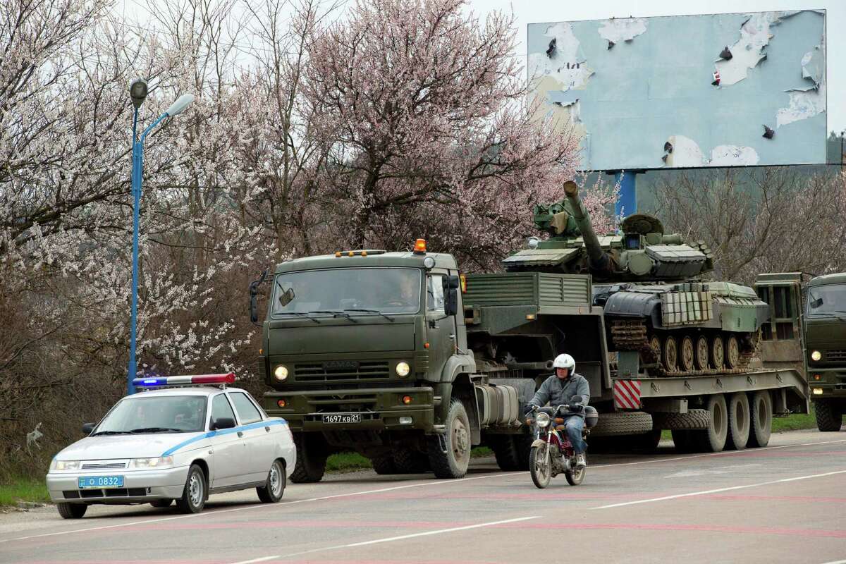 A man on a motorcycle passes by Ukrainian tanks as they are transported from their base in Perevalnoe, outside Simferopol, Crimea, Wednesday, March 26, 2014. Ukraine has started withdrawing its troops and weapons from Crimea, now controlled by Russia. (AP Photo/Pavel Golovkin)