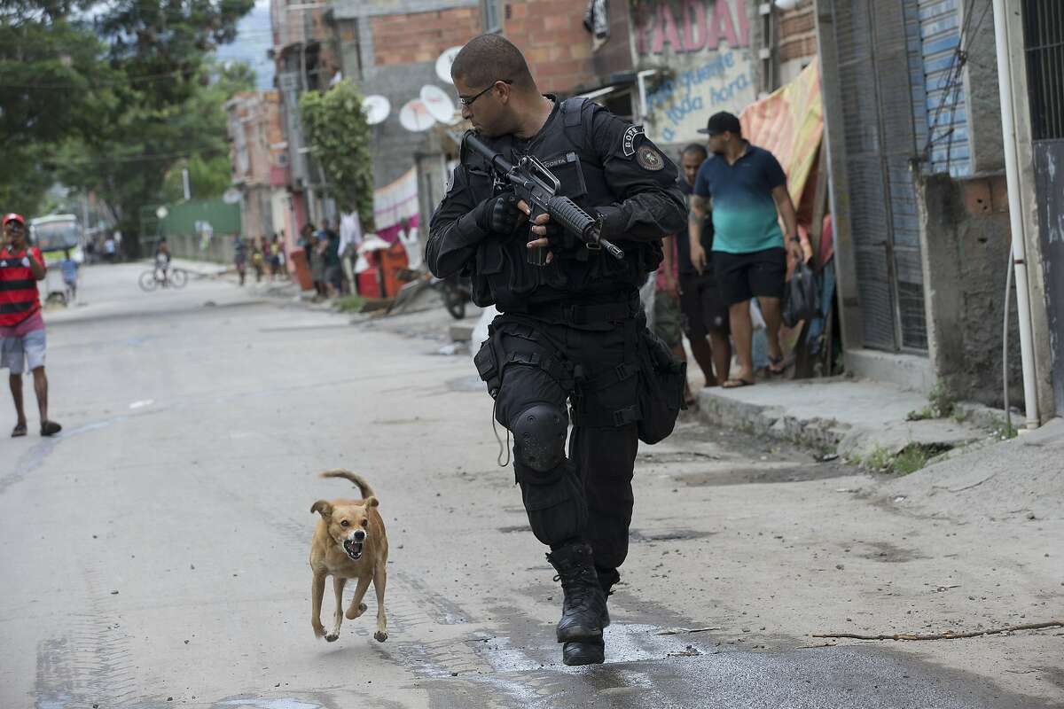 A Special Police Operations Battalion (BOPE) officer is chased by a barking dog during an operation in the Mare slum complex, ahead of its "pacification," in Rio de Janeiro, Brazil, Wednesday, March 26, 2014. Elite federal police and army troops will be sent to the city to help quell a wave of violence in so-called "pacified" slums. Recent attacks on police bases in the favelas is raising concerns about an ambitious security program that began in 2008, in part to secure the city ahead of this year's World Cup and the 2016 Olympics. (AP Photo/Silvia Izquierdo)