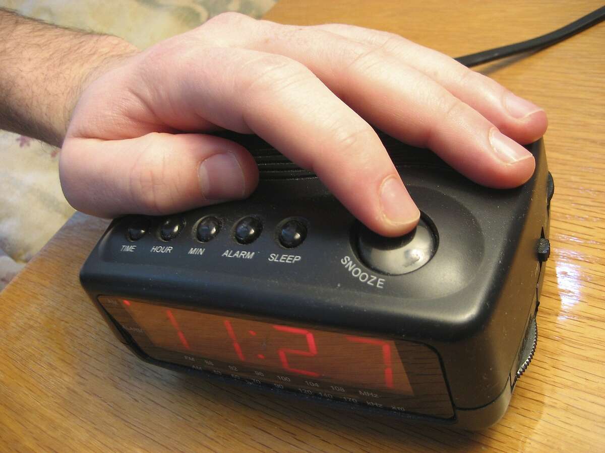 Hand reaching to press the snooze button on an alarm clock