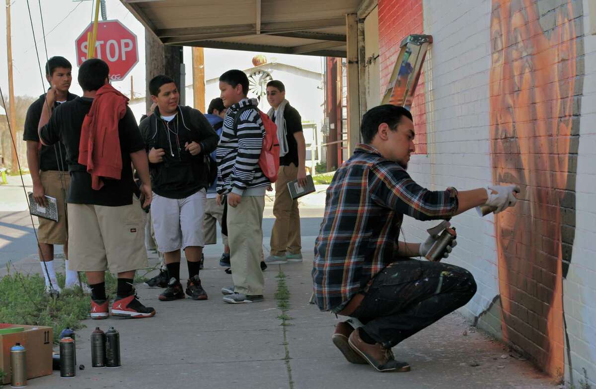 ABOVE: A group of young people gather as San Antonio artist Christopher Montoya, 21, puts the finishing touches on his giant mural honoring Cesar Chavez, the late labor organizer. AT LEFT: The colorful mural honoring Chavez is at the corner of South Flores and Pruitt. Montoya is a graduate of Brackenridge High.
