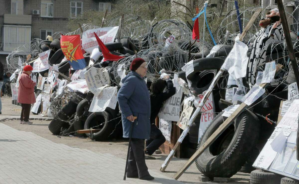 Women read banners as they pass the barricades of pro-Russian activists at a regional administration building that they had seized earlier in Donetsk, Ukraine, Tuesday, April 15, 2014. Several government buildings have fallen to mobs of Moscow loyalists in recent days as unrest spreads across the east of the country.