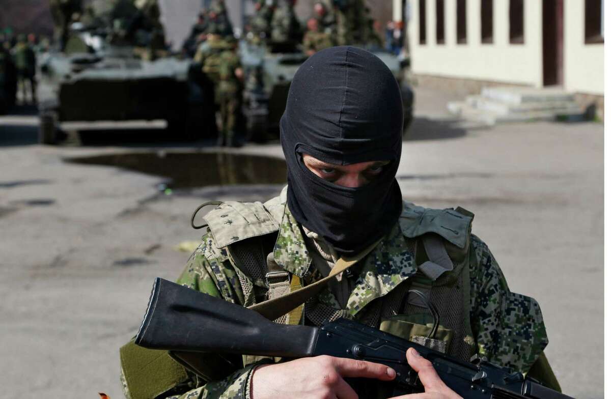 A masked gunman guards combat vehicles with Russian, Donetsk Republic and Ukrainian paratroopers, flags and gunmen on top, parked in downtown of Slovyansk on Wednesday, April 16, 2014. The troops on those vehicles wore green camouflage uniforms, had automatic weapons and grenade launchers and at least one had the St. George ribbon attached to his uniform, which has become a symbol of the pro-Russian insurgency in eastern Ukraine. (AP Photo/ Sergei Grits)