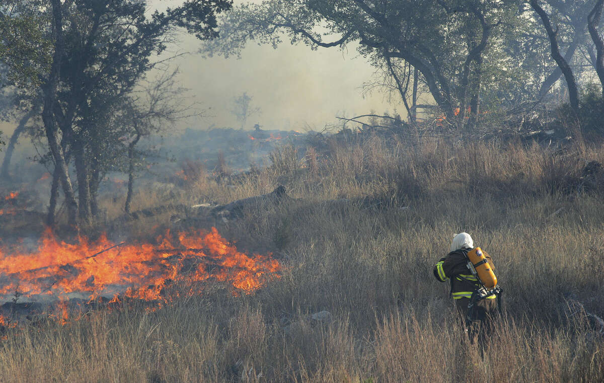 Surrounded by dried grass, a member of the City of Shavano Park Fire Department works a major brush fire in northern Bexar County north of San Antonio on Thursday, Jan. 5, 2006. Residents of the Fossil Ridge subdivision, south of the fire, were asked to evacuate due to the danger. Fire departments from throughout the county were involved in the firefighting effort.