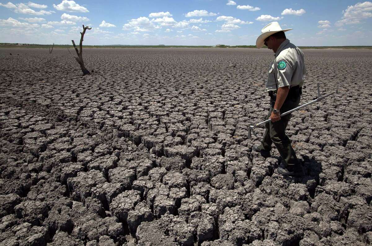 FILE - In this Aug. 3, 2011 file photo, Texas State Park police officer Thomas Bigham walks across the cracked lake bed of O.C. Fisher Lake in San Angelo, Texas. Global warming is rapidly turning America into a stormy and dangerous place, with rising seas and disasters upending lives from flood-stricken Florida to the wildfire-ravaged West, according to a new U.S. federal scientific report released Tuesday, May 6, 2014. (AP Photo/Tony Gutierrez)