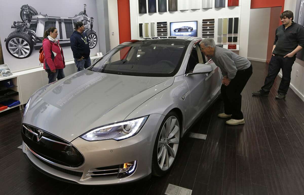 In this March 17, 2014 file photo, Tesla representative John Van Cleave, right, shows customers Sarah and Robert Reynolds, left, and Vince Giardina, a new Tesla all electric car, at a Tesla showroom inside the Kenwood Towne Centre in Cincinnati.