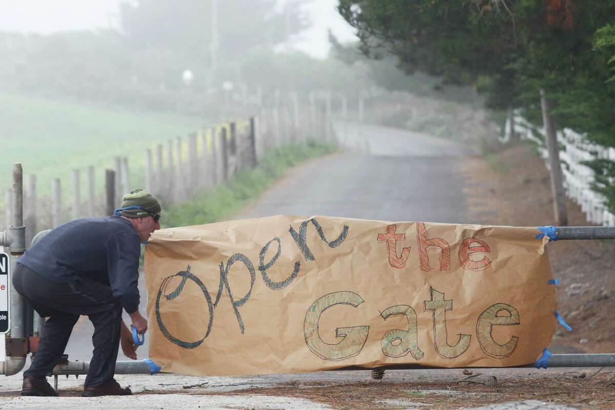 Protester Tom Wilhelm puts a sign on the gate at Martins Beach Road in March.