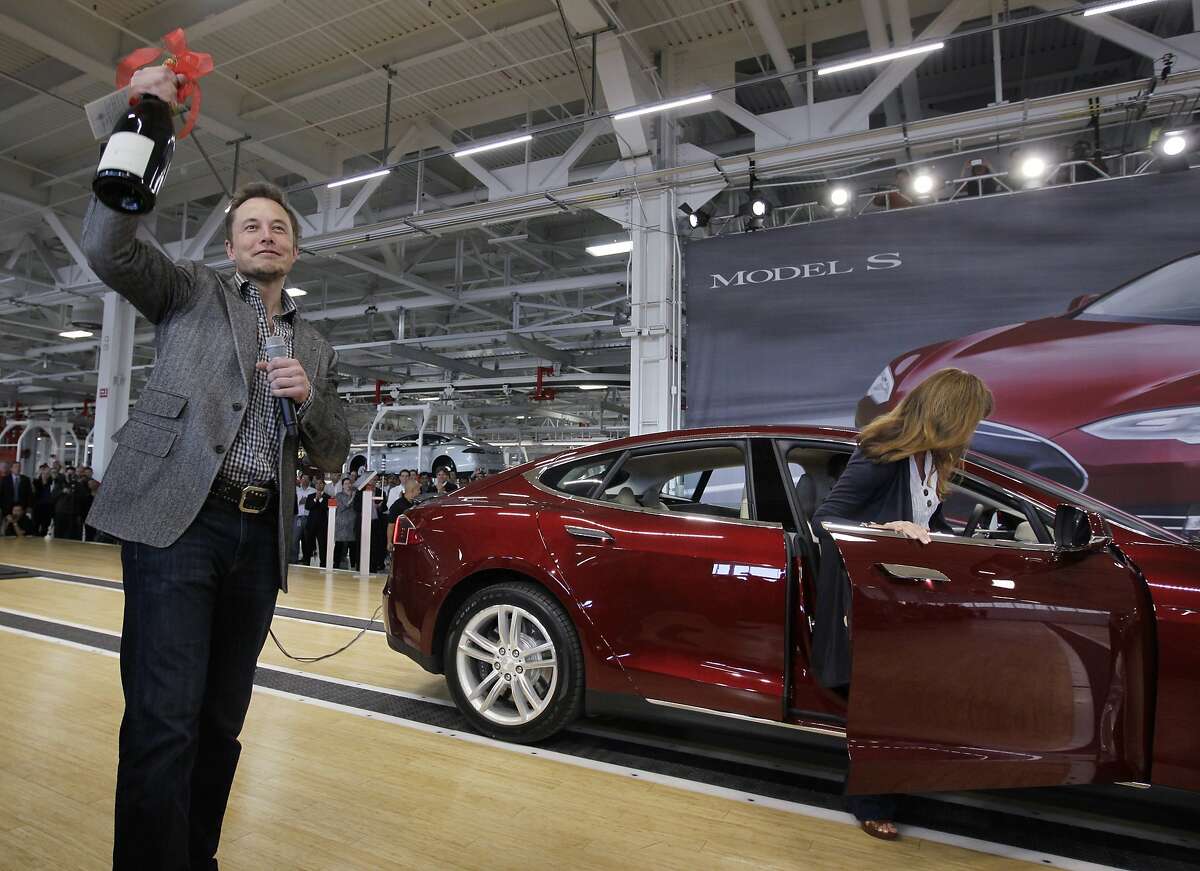 Tesla CEO Elon Musk holds up a bottle of wine as a gift from one of the first customers, right, during a rally at the Tesla factory in Fremont, Calif., Friday, June 22, 2012. The first mass-market sedans offered by electric car maker Tesla are now on the road. (AP Photo/Paul Sakuma)