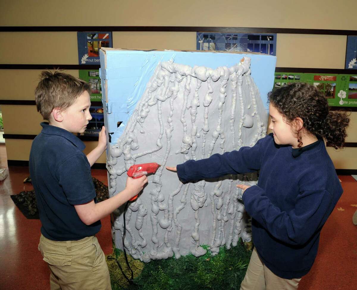 Robert Blair, a member of Walnut Bend Elementary School's Odyssey of the Mind team, uses a wax gun for finishing touches on a volcano that he created as part of the team's display for the event's world competition in Ames, Iowa. Offering suggestions is fellow team member Daniela Perez. The team won regional and state level competitions with their weight-bearing project.