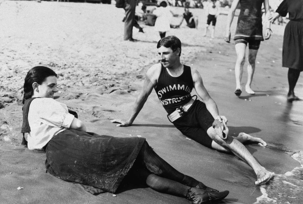 Portrait of a bathing suit-clad woman and a swimming instructor lying close to the surf on Midland Beach, Staten Island, New York, 1898.