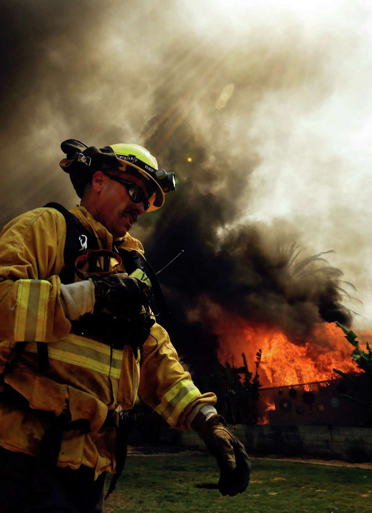 A firefighter moves past a burning structure during a wildfire Thursday, May 15, 2014, in Escondido, Calif. One of the nine fires burning in San Diego County suddenly flared Thursday afternoon and burned close to homes, trigging thousands of new evacuation orders. (AP Photo/Gregory Bull)