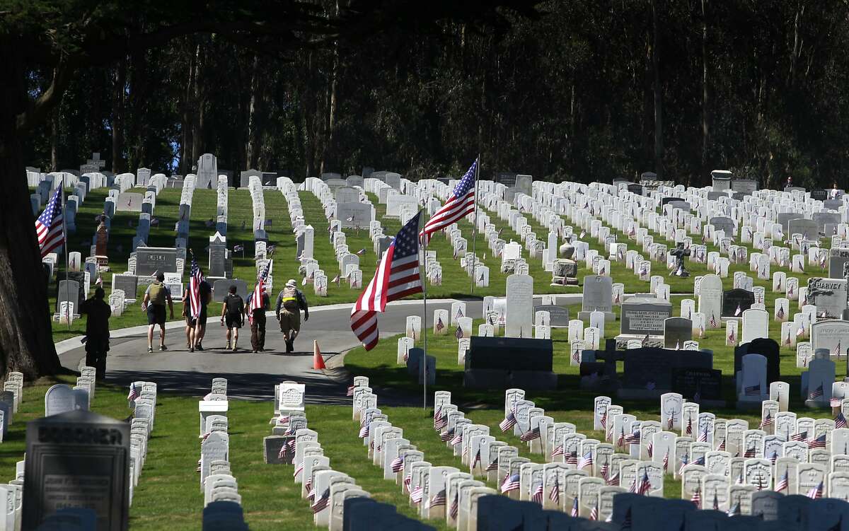 Visitors walk with U.S. flags at the National Cemetery of The Presidio during the Memorial Day Ceremony in San Francisco, Calif. on Monday, May 26, 2014.