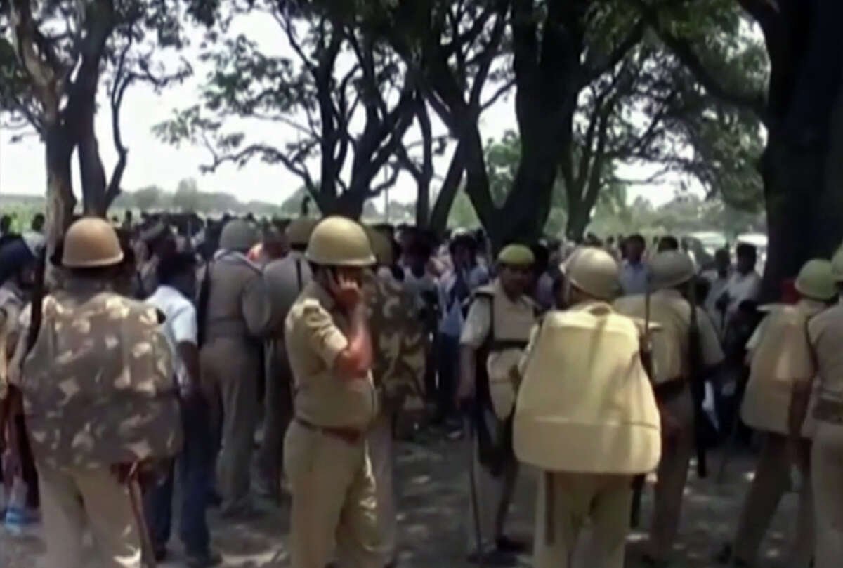 In this Wednesday, May 28, 2014 image taken from video, police stand amongst the crowd near where two teenage sisters were found hanging from a mango tree in the Katra village in Uttar Pradesh state, in northern India. Authorities have arrested three men, including two police officers, suspected of gang-raping and killing the teenagers before hanging their bodies from the tree, sparking renewed public outrage over sexual violence in the country. (AP Photo/NNIS via AP Video) INDIA OUT
