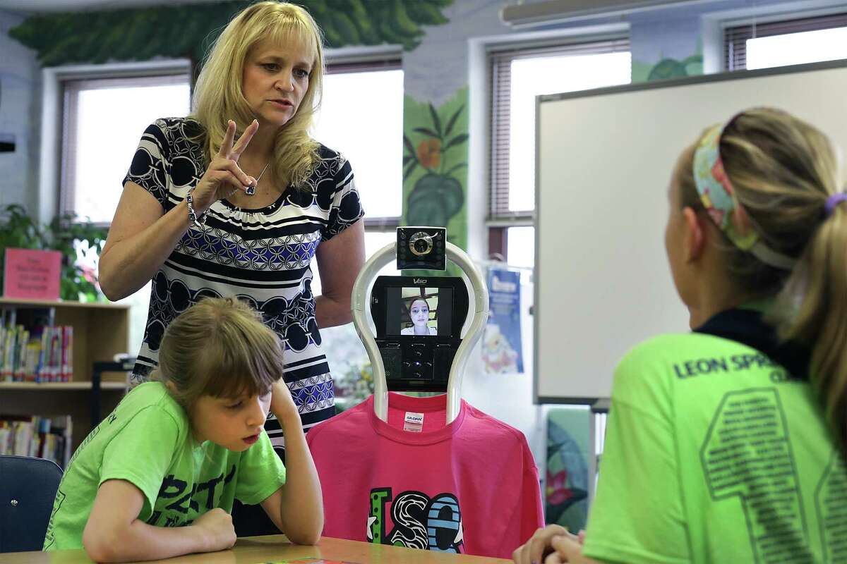Joy Ulcak, top left, 5th grade teacher at Leon Springs Elementary School, assists students Caitlin Clark, left, Abby Murry, right, and Rebecca Taylor, center, during an educational game. Taylor has been home bound much of this year due to an illness, but she can still participate in classroom learning through the use of a robot she can control from home, Wednesday, June 4, 2014.