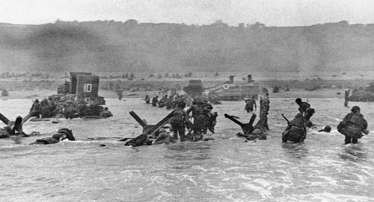 FILE - In this June 6, 1944 file picture, some of the first assault troops to hit the Normandy, France beachhead take cover behind enemy obstacles to fire on German forces as others follow the first tanks plunging through the water towards the German-held shore during World War II. (AP Photo)