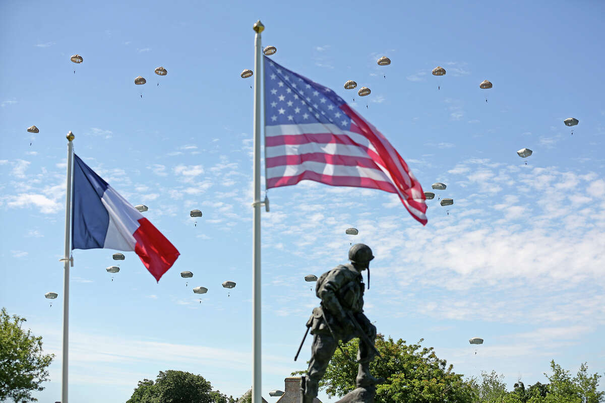 Paratroopers are dropped near the Normandy village of Sainte Mere Eglise, western France, during a mass air drop, Sunday June 8, 2014, as part of commemorations of the 70 anniversary of the D-Day landing. World leaders and veterans gathered by the beaches of Normandy on Friday to mark the 70th anniversary of the World War II D-Day landings. Visible at foreground is bronze sculpture Iron Mike, a monument dedicated to the American airborne soldiers who fought on the D Day.