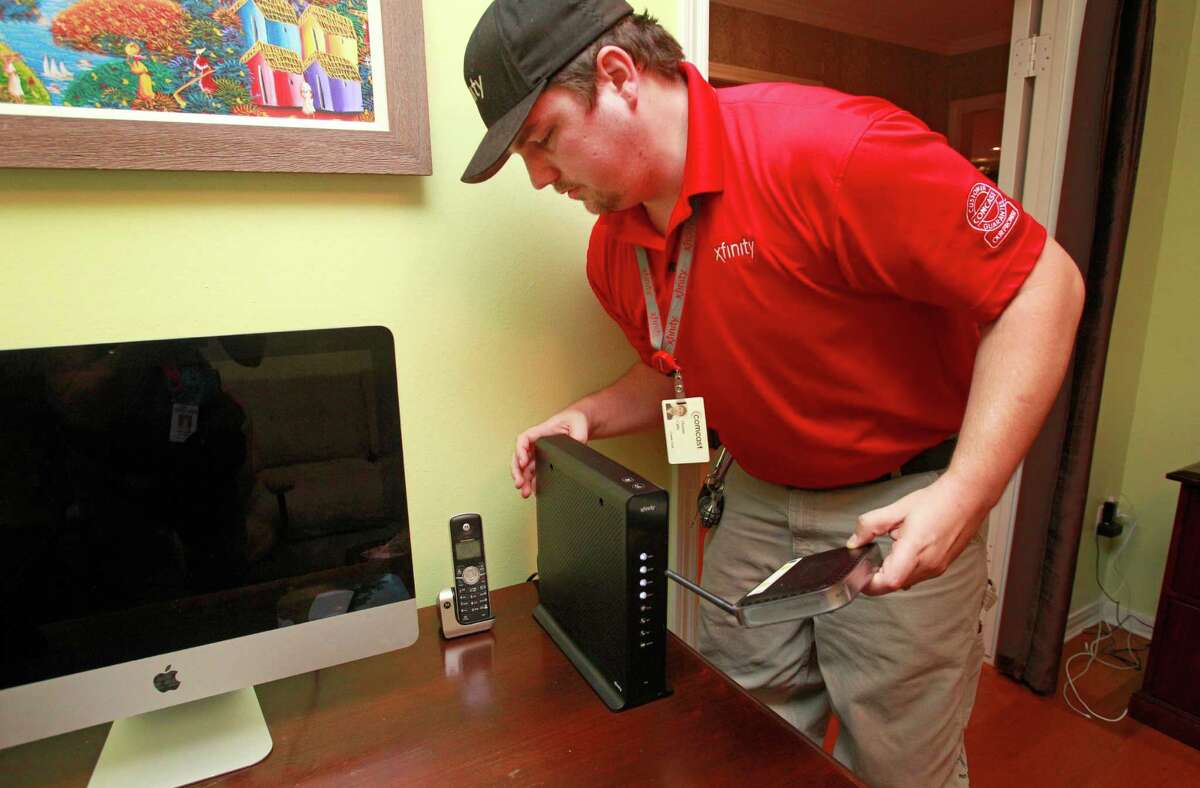 Comcast technician Thomas Cable installs a wireless gateway in a Houston home in this 2014 file photo. Comcast's combined cable modems and routers cost $10 a month to rent, but you can save over time by buying your own equipment.