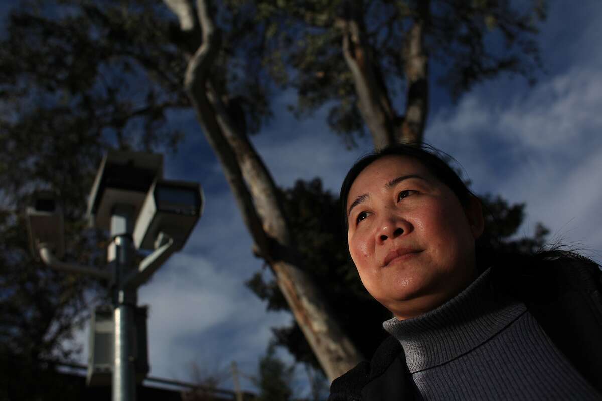 In this file photo, Phuong Nguyen of Oakland stands near a red light camera unit at the 27th St. on ramp to I-580 at Northgate Avenue in Oakland. Nguyen periodically works at her family's flower store, MP Flowers, on 27th Avenue and says 3 family members have gotten tickets at the corner.