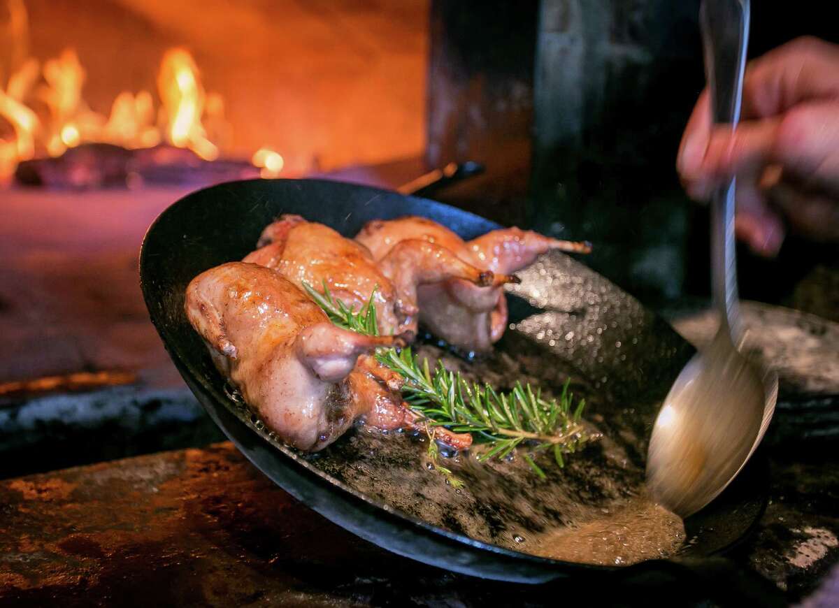 A cook bastes quail roasting in the wood oven at Molina in Mill Valley.