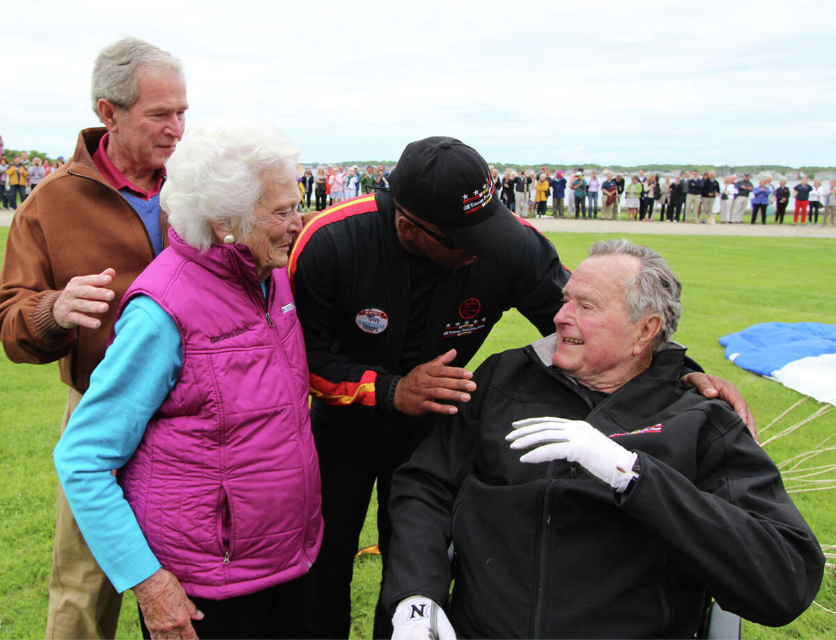 In this photo provided by the All Veteran Parachute Team, former President George H.W. Bush, right, is congratulated on his parachute jump by his son, former President George W. Bush, far left, his wife Barbara Bush and his tandem team partner Mike Elliott on his 90th birthday in Kennebunkport, Maine, Thursday, June 12, 2014. (AP Photo/All Veteran Parachute Team, Kenneth Wasley)