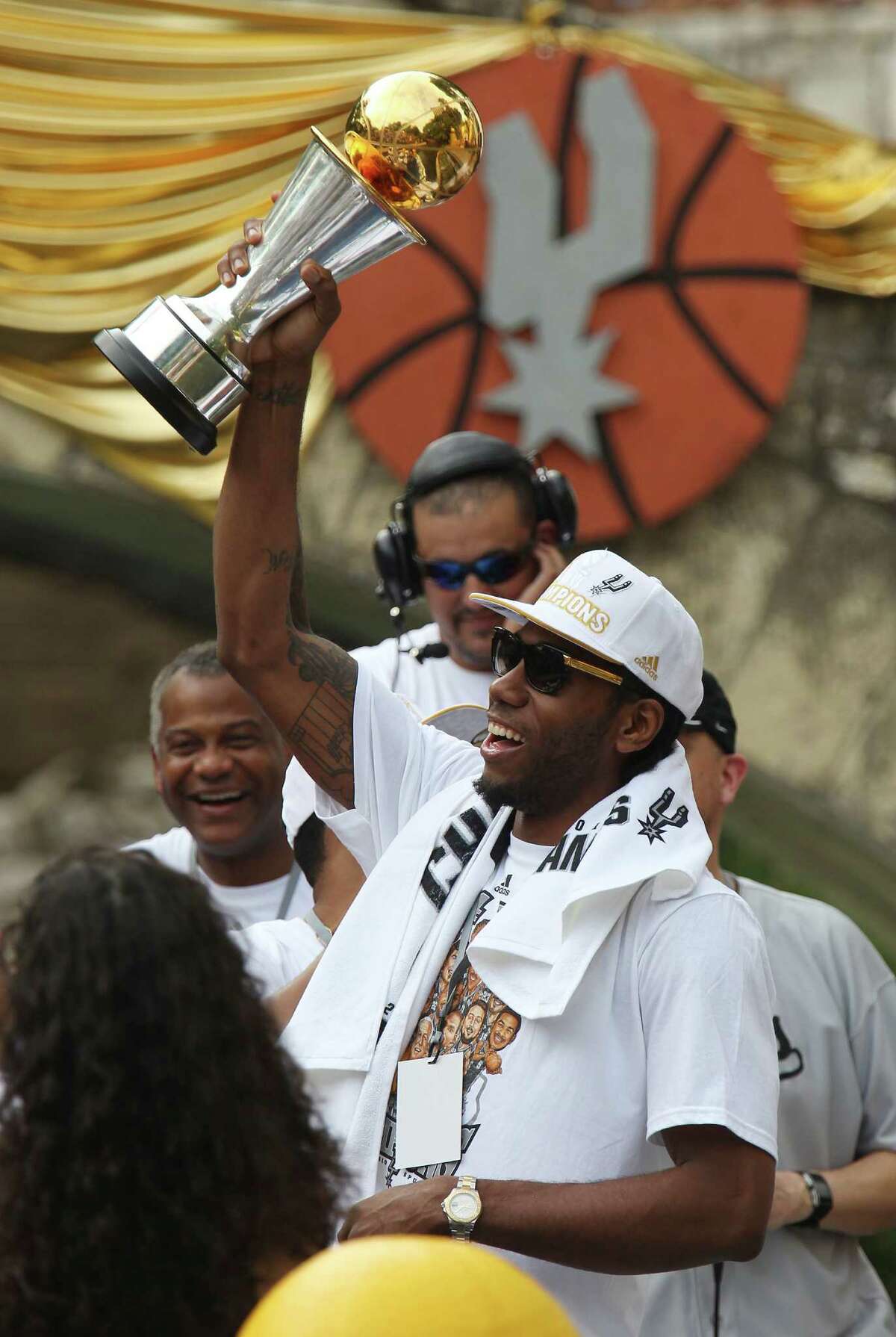 San Antonio Spurs' Kawhi Leonard hoists up the MVP Trophy during the river parade for the San Antonio Spurs after the team capture their fifth NBA championship on Wednesday, June 18, 2014.