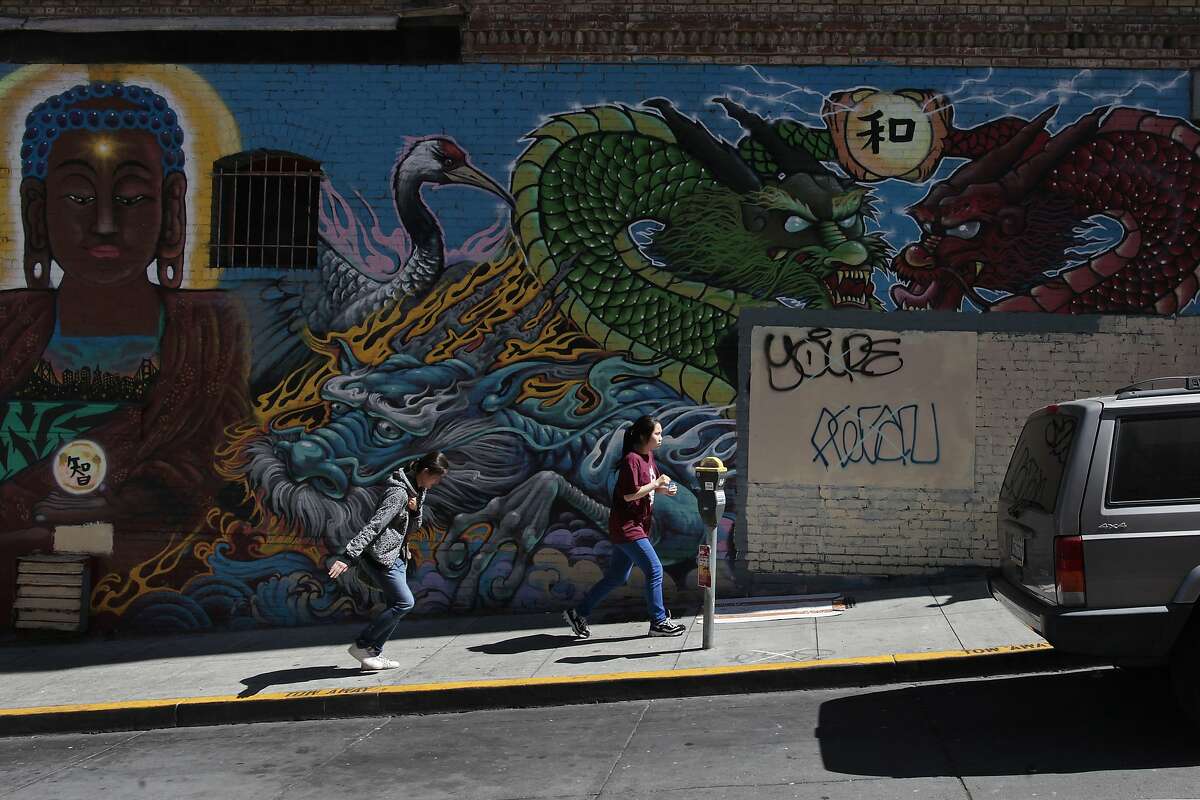 Two women run by a mural that used to have a Banksy piece on it on Commercial St. in San Francisco, Calif. on Thursday, June 19, 2014. San Francisco is home to several Banksy pieces.
