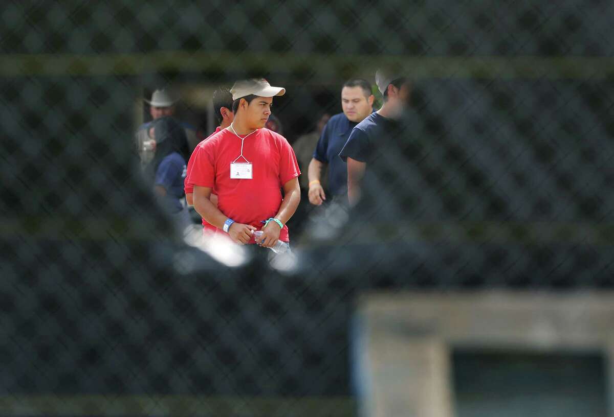 Young male immigrants can be seen through a wind flap on a screened off fence at the old housing facilities at Lackland Air Force Base. Texas Attorney General Greg Abbott and U.S. Senator Ted Cruz addressed members of the media following their tour of the facilities housing young immigrants at Lackland Air Force Base in San Anotnio, TX, Monday, June 23, 2014. U.S. Rep. Michael Burgess also went on the tour.