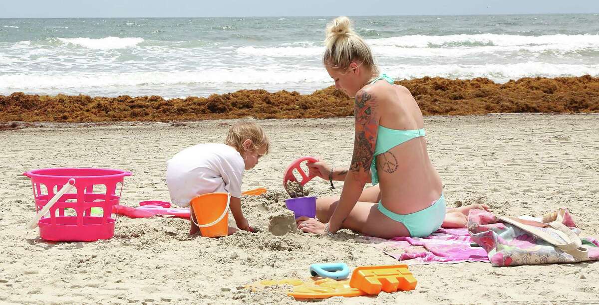 Katelyn Lowery right, and her 23 month-old daughter Johnsie Lowery play in the sand as mounds of seaweed build up on the beach near 21st street Thursday, May 22, 2014, in Galveston.