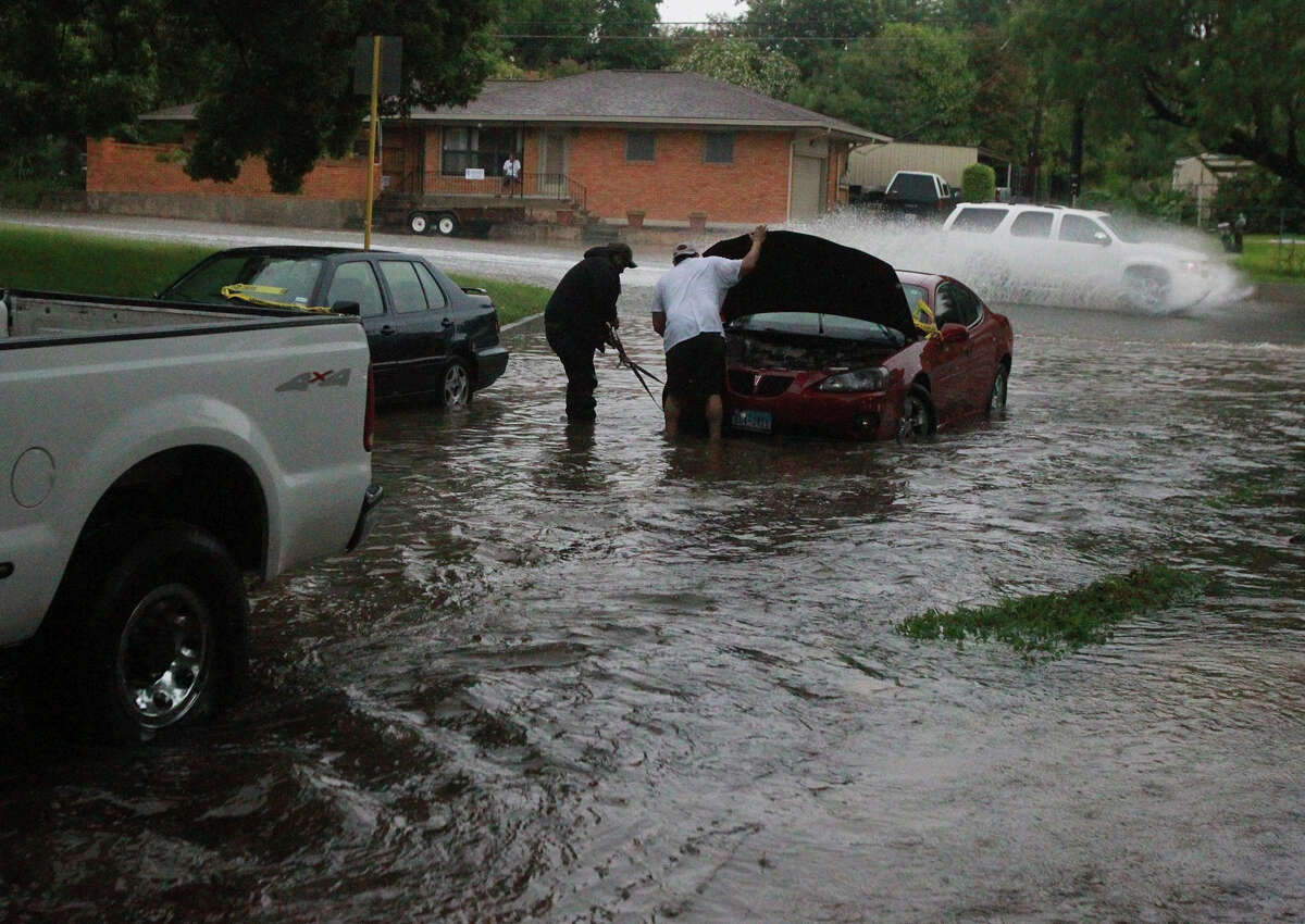 Raymond Martinez (center, white t-shirt) prepares to have his car towed Wednesday June 25, 2014 at Brightwood Place and N. New Braunfels after stalling in high water.